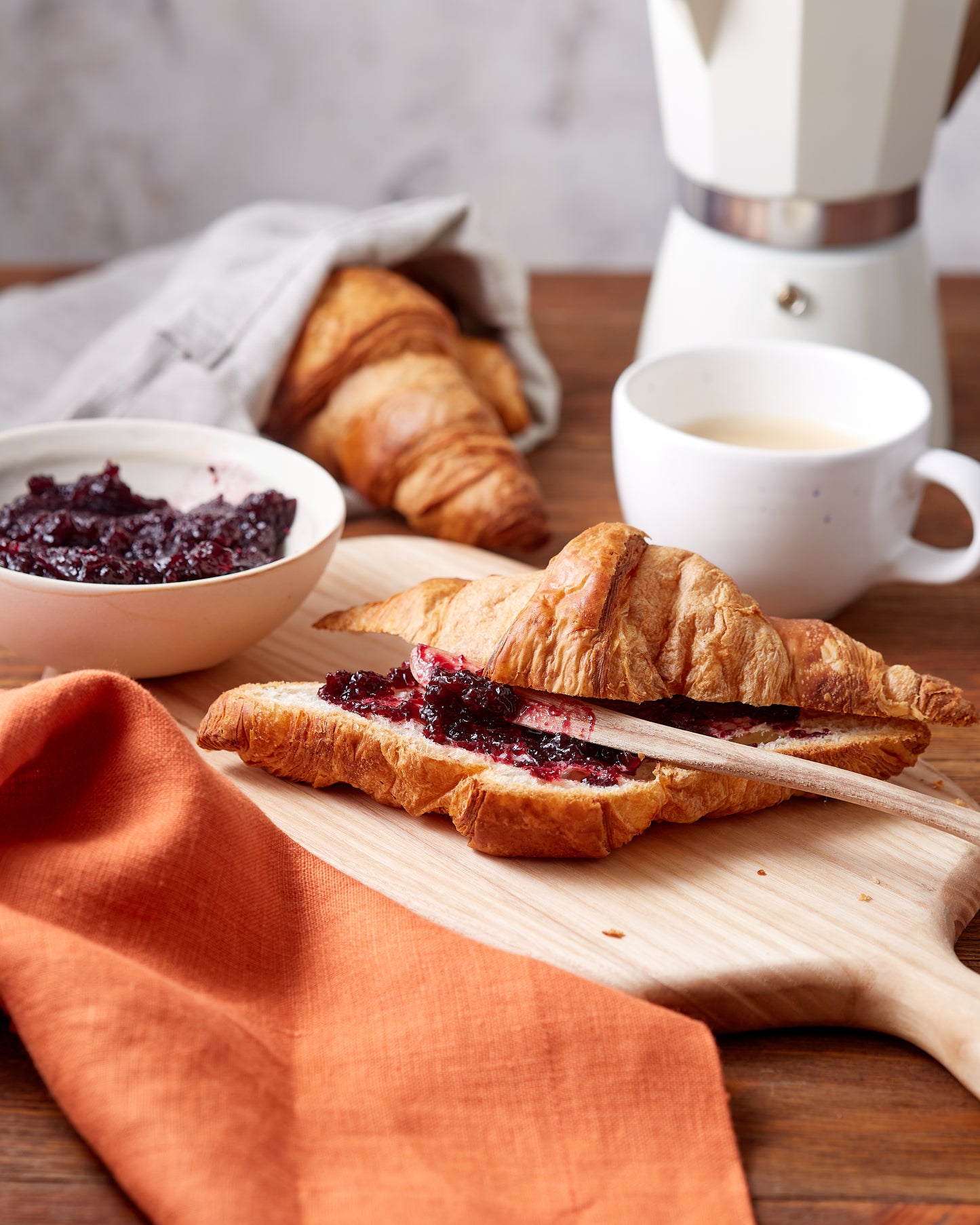 Croissants with jam on a wooden board, accompanied by a bowl of jam and a cup of coffee, fall breakfast styled with linen napkin