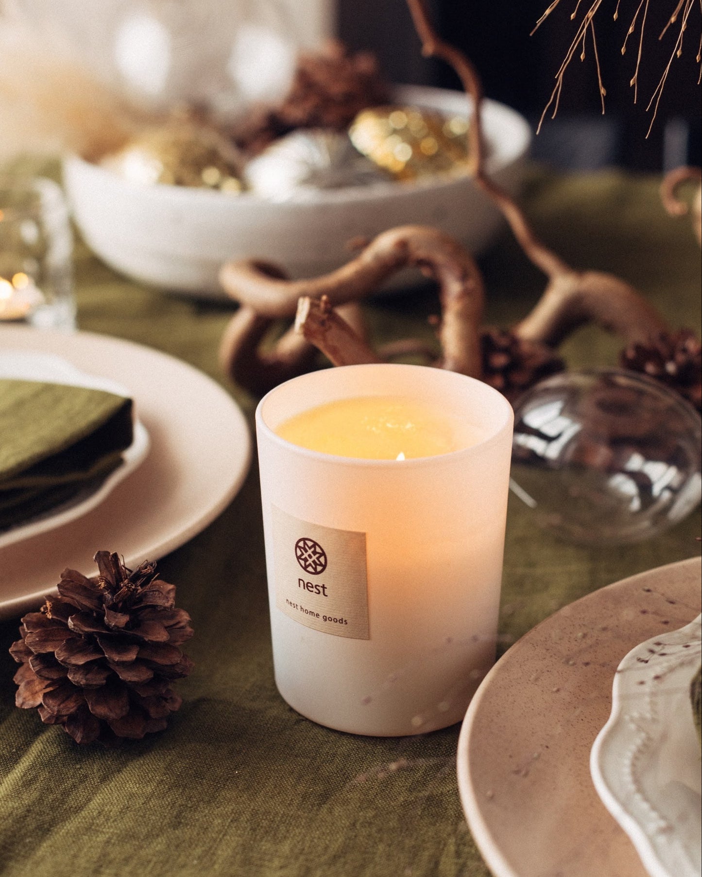 Candle on a table with decorative elements including a pine cone and branches, styled by a table stylist and product designer Iryna Kolosvetova