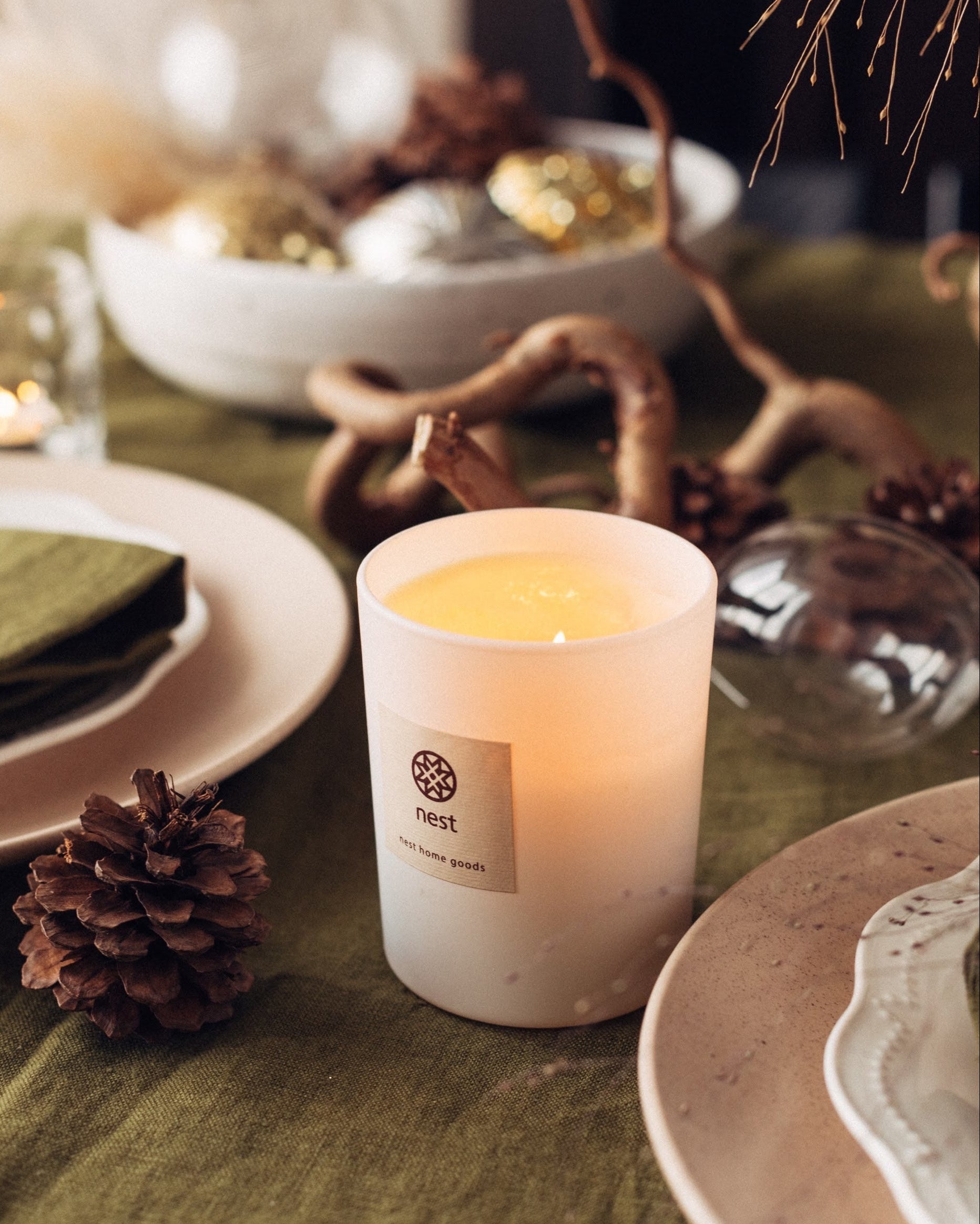 Candle on a table with decorative elements including a pine cone and branches, styled by a table stylist and product designer Iryna Kolosvetova