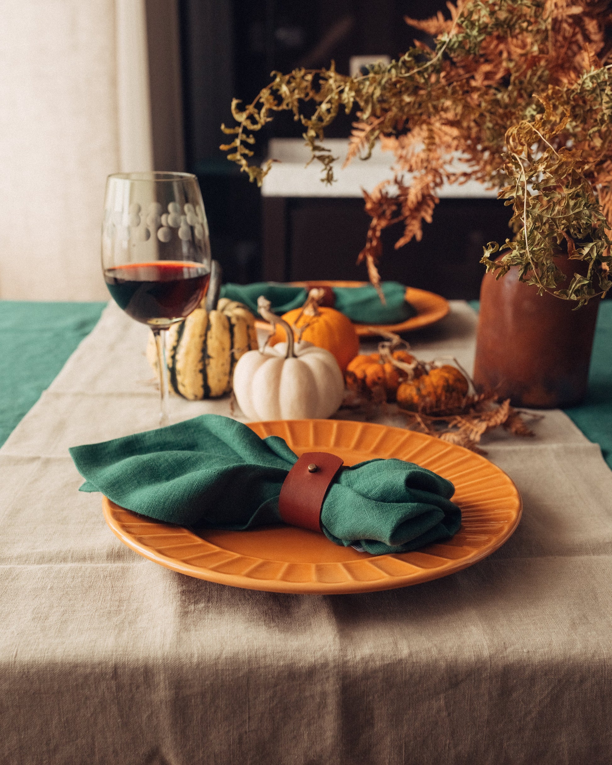 Table setting with orange plates, green napkins, and pumpkins on a beige tablecloth. Styled by Iryna Kolosvetova for Fine Dining 4 Home