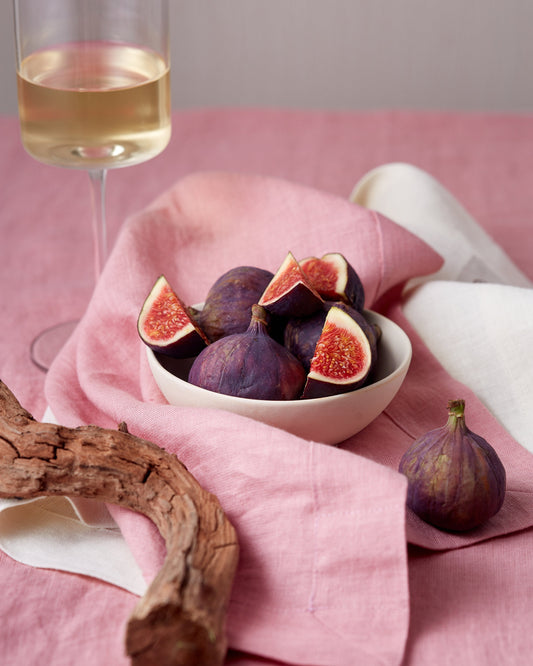 Summer table setting with vibrant linen table runner and napkins, fresh figs in the bowl and glass of white wine