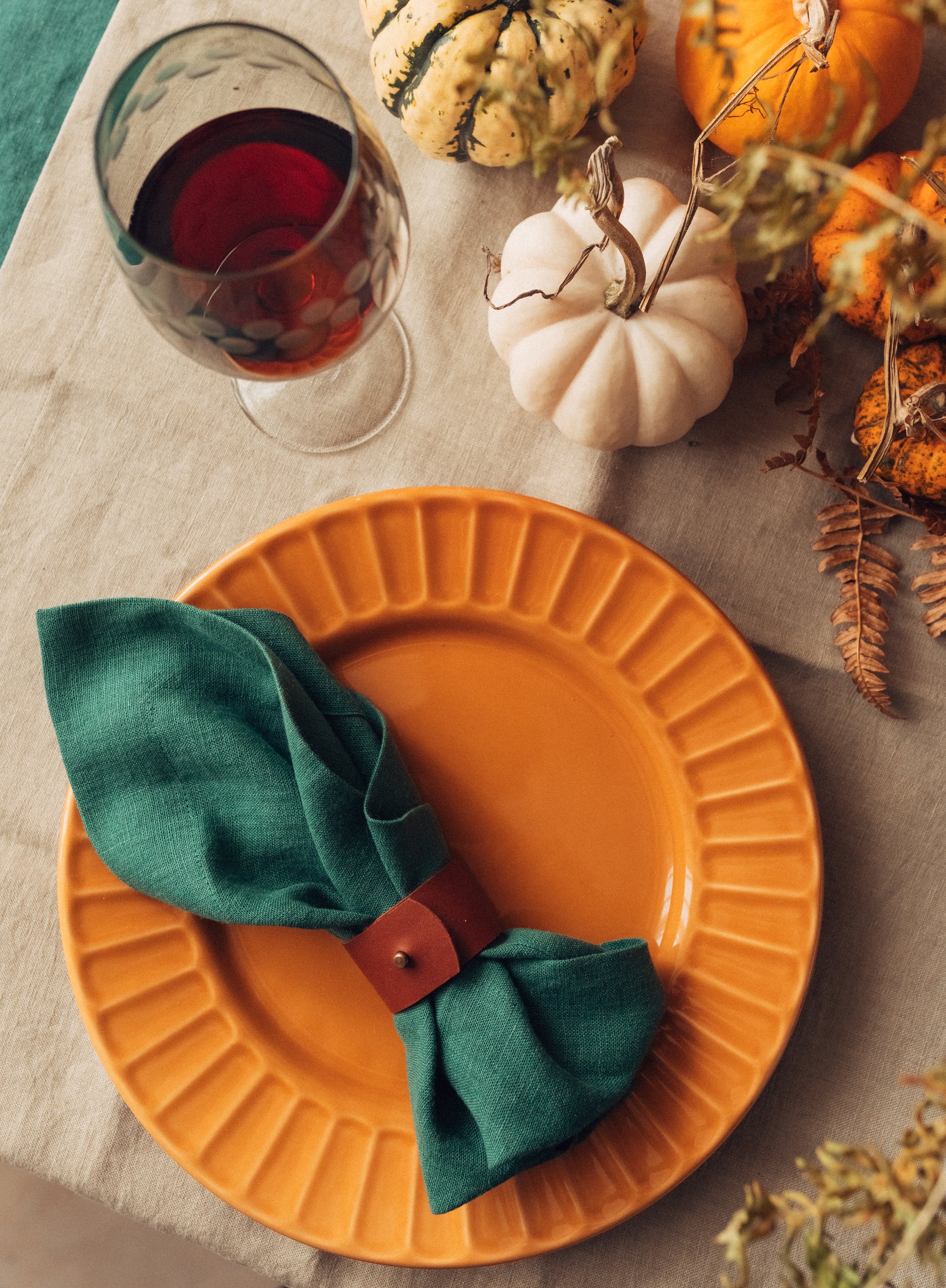 Orange plate with a green napkin and red buckle, surrounded by pumpkins and autumn decorations.