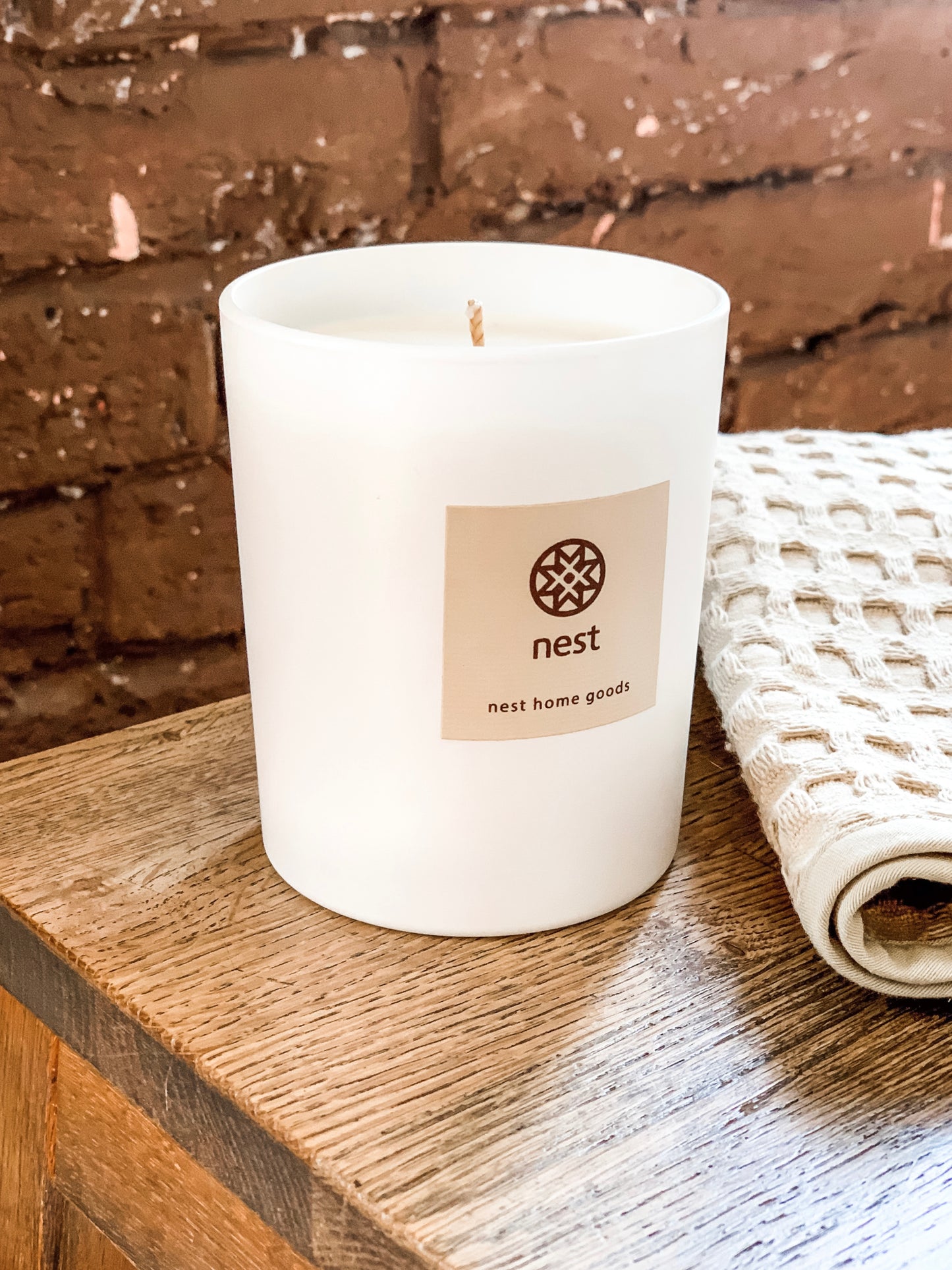 White candle on wooden surface against a brick wall. Nest Home Goods collection for Fine Dining for Home