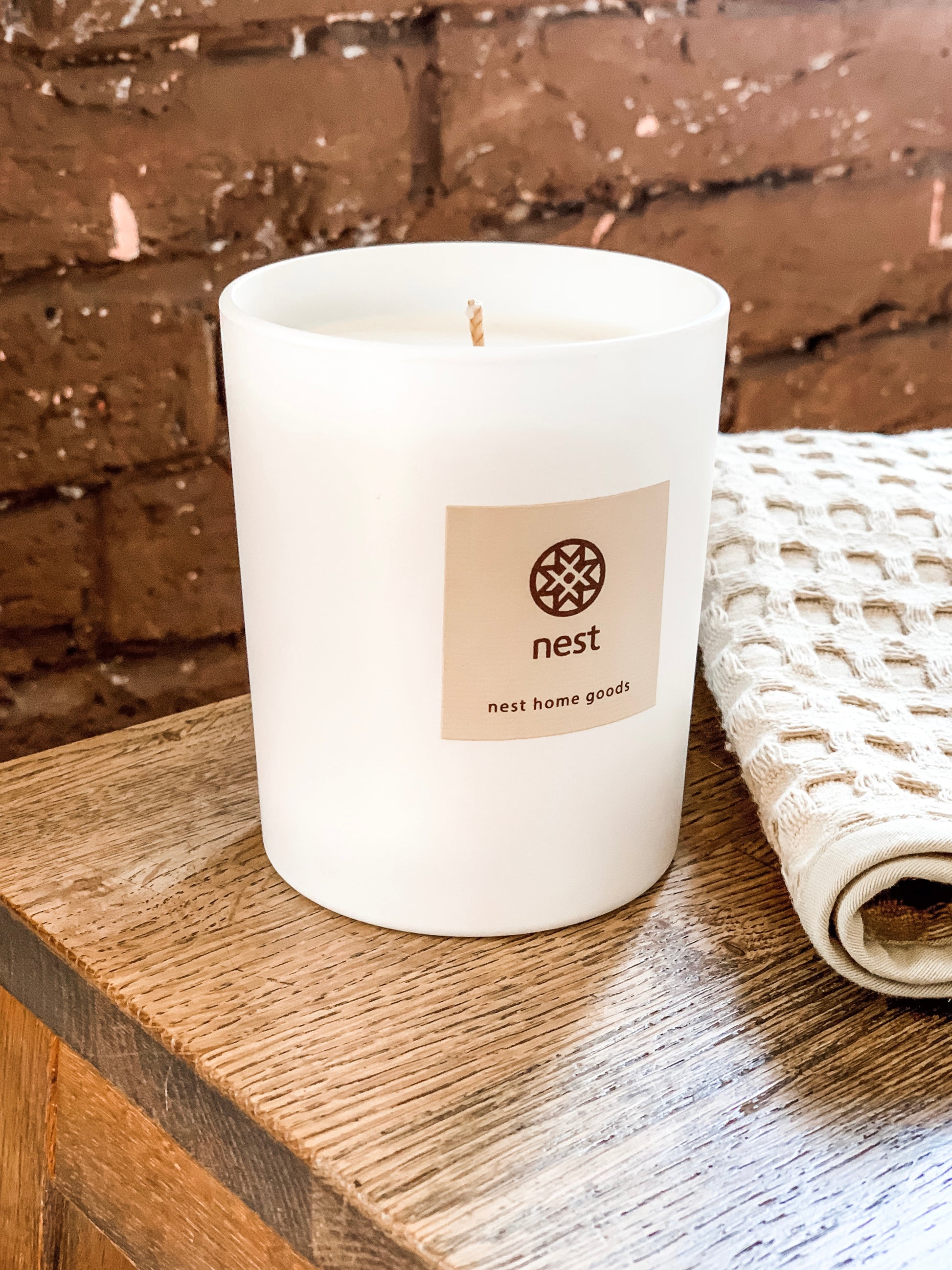 White candle on wooden surface against a brick wall. Nest Home Goods collection for Fine Dining for Home
