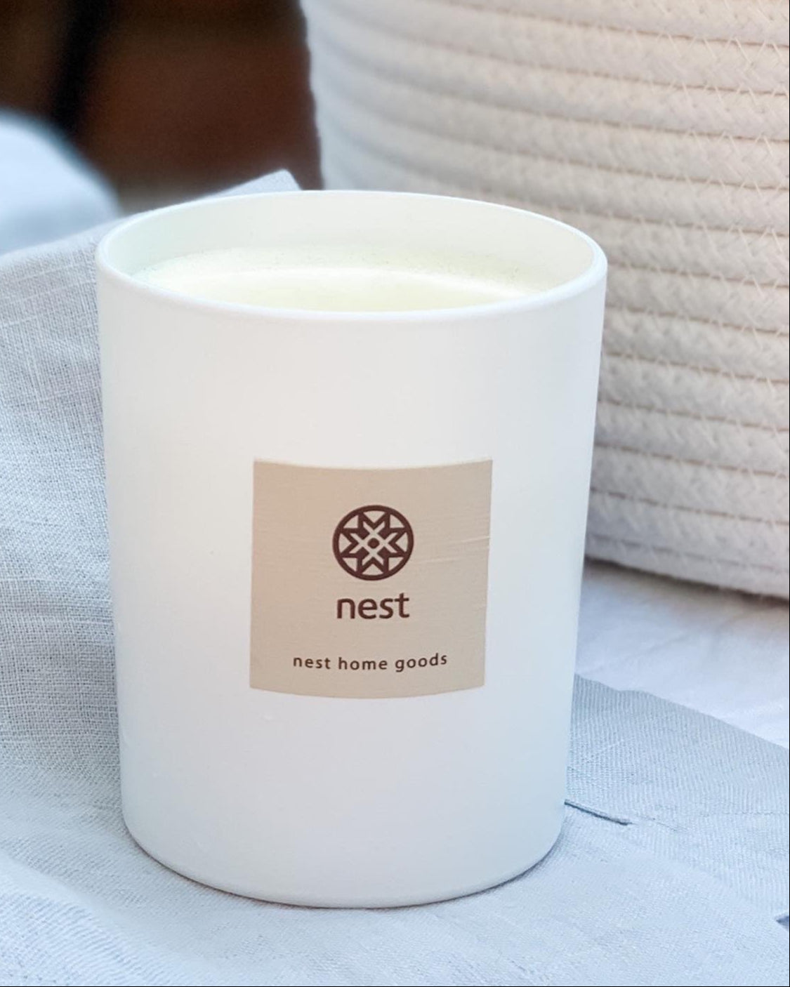White candle with 'nest home goods' label on a light linen surface